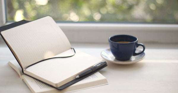 Cozy workspace setup with open notebook and coffee near a sunlit window. Photo by Bedia on Pexels.