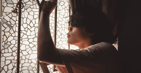 Side view of a young man posing thoughtfully by a mosaic glass window with soft light. Photo by Minh Đức on Pexels.