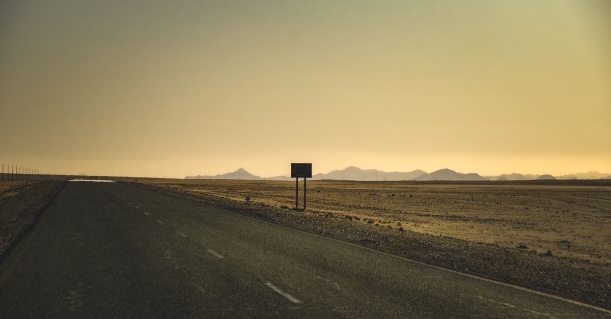 A serene view of an empty road stretching through a desert at sunset with distant mountains. Photo by Francesco Ungaro on Pexels.