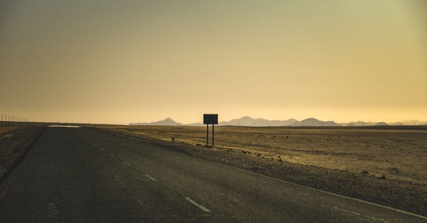 A serene view of an empty road stretching through a desert at sunset with distant mountains. Photo by Francesco Ungaro on Pexels.
