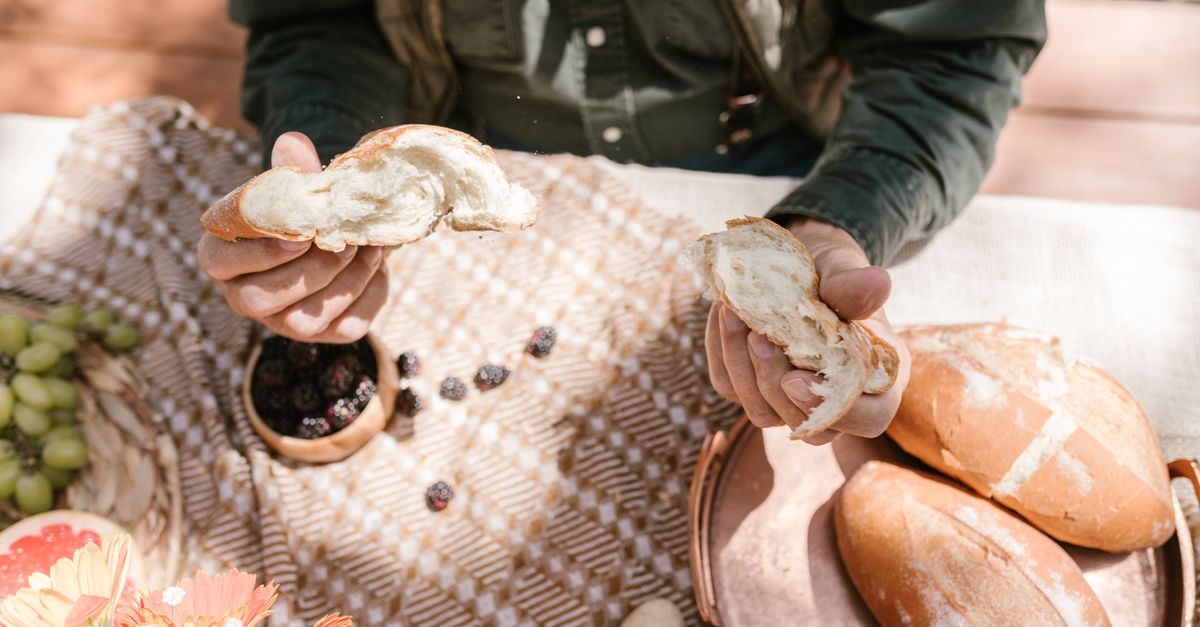 A person at an outdoor picnic holding fresh bread with seasonal fruits and flowers. Photo by RDNE Stock project on Pexels.